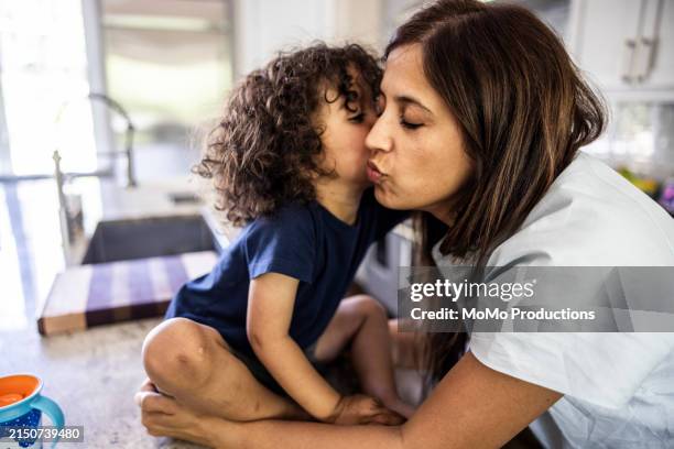 mother kissing toddler boy in kitchen - boy blue stock pictures, royalty-free photos & images