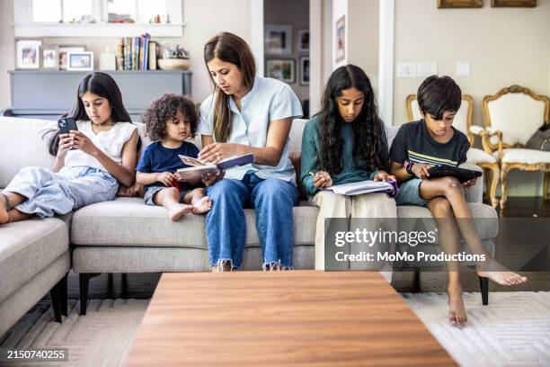 mother and children reading and using devices on sofa at home - screen time stock pictures, royalty-free photos & images