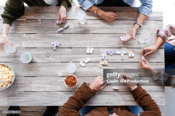 overhead view unrecognizable adults playing dominoes and eating snacks - dominos game stock pictures, royalty-free photos & images