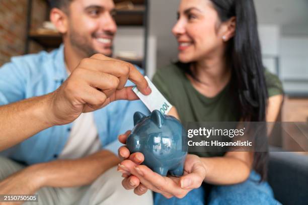 couple at home saving money in a piggybank - savings stock pictures, royalty-free photos & images