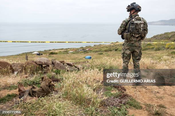 Mexican marine stands guard as rescue workers, forensics, and prosecutors work in a waterhole where human remains were found near La Bocana Beach,...