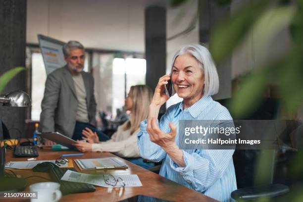 successful business deal for older manager working in office. beautiful mature woman making phone call. age diverse team concept. - retraités qui travaillent photos et images de collection