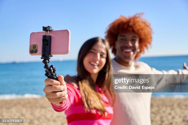 cheerful multiracial friends showing their family the beach via video call - selfiestick stockfoto's en -beelden