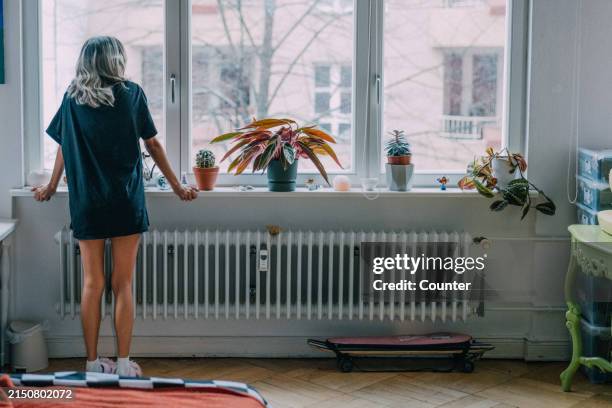 woman looking out of window at home in the morning - berlin winter stock pictures, royalty-free photos & images