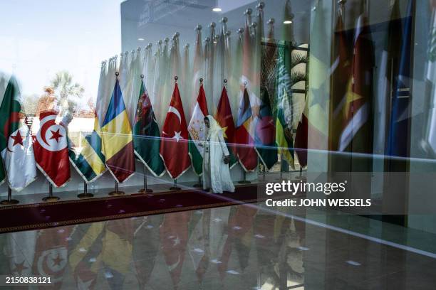 Delegate walks past member state flags inside the Sir Dawda Kairaba Jawara International Conference Center during the Organisation of Islamic...