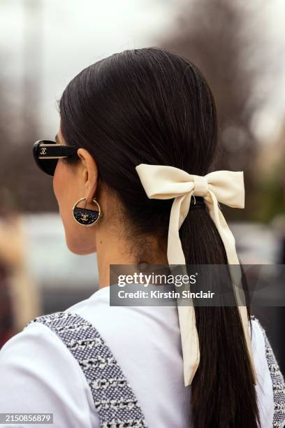 Mehrnaz Ansari wears Chanel sunglasses, earrings, playsuit and T shirt with a cream bow in her hair outside the Chanel show during the Womenswear...