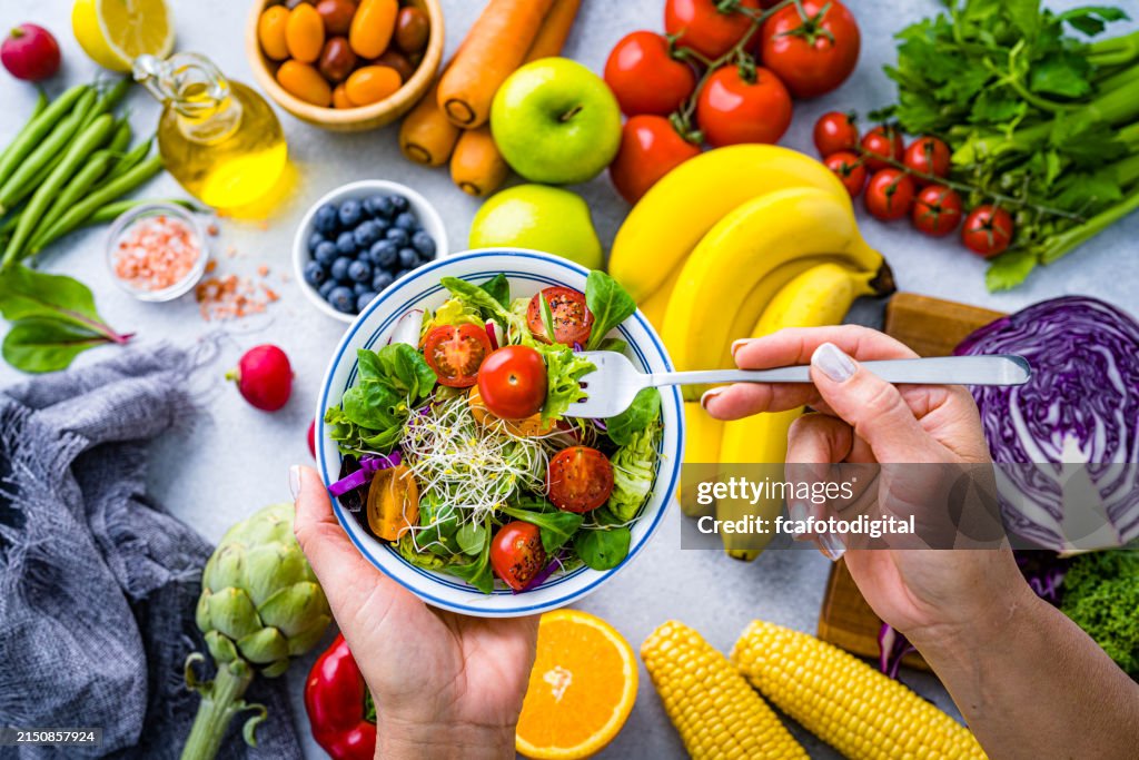 Frau isst frischen regenbogenfarbenen Salat. Mehrfarbiger Obst- und Gemüsehintergrund. Gesundes Ernährungs- und Diätkonzept