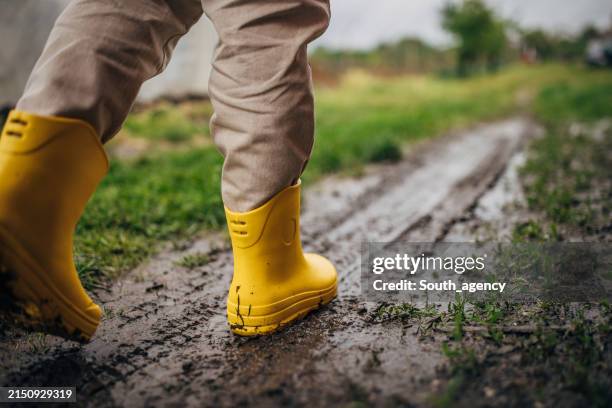 person wearing yellow boots on muddy ground - laarzen geel stockfoto's en -beelden