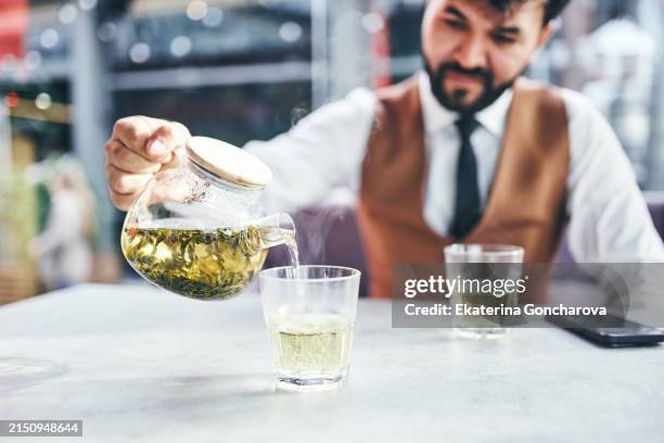 confident man pouring green tea in a stylish setting, focus on the action and elegance - white tea extract stock pictures, royalty-free photos & images
