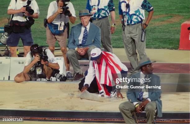 Photographers crowd American athlete Carl Lewis, draped in an American flag, as he collects sand from the pit after winning the men's long jump final...