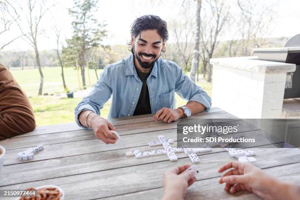 young man smiles before placing winning domino - dominos game stock pictures, royalty-free photos & images