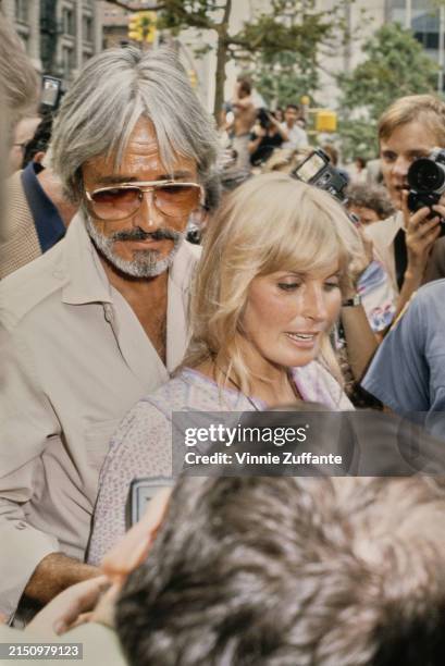 American actor and film director John Derek, wearing a beige shirt, and his wife, American actress Bo Derek, who wears a purple-and-white patterned...