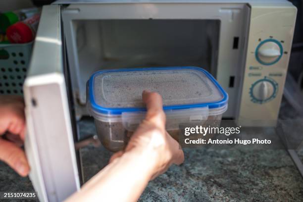 woman's hand putting a tupper with food to heat in microwave. - putting food in microwave stock-fotos und bilder