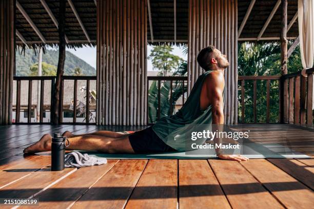 side view of man practicing cobra pose on exercise mat at wellness resort - cobra pose stock pictures, royalty-free photos & images