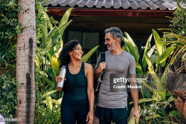 smiling mature couple walking amidst plants at wellness resort - vida activa fotografías e imágenes de stock