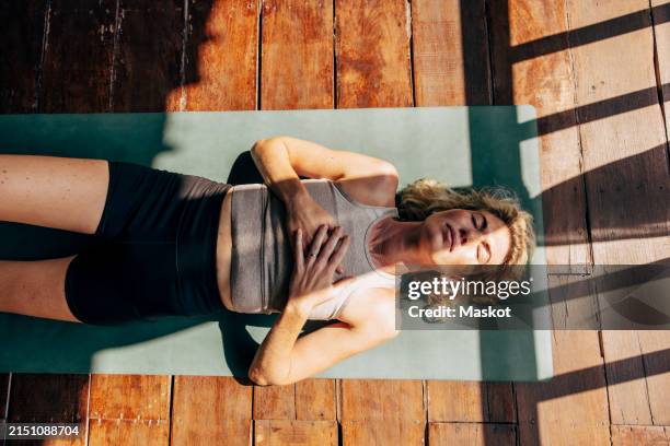 directly above shot of woman lying down on yoga mat with hands on chest at wellness resort - yoga stockfoto's en -beelden