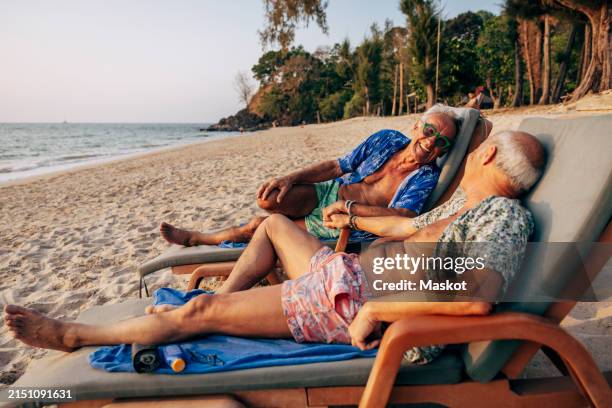 happy senior gay couple reclining on deck chair at beach during vacation - liegestuhl stock-fotos und bilder