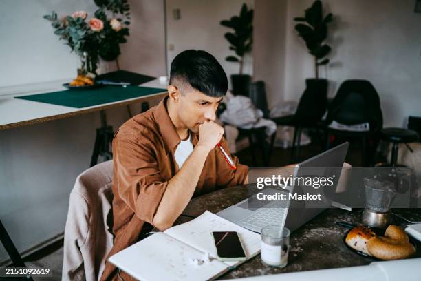 thoughtful male business professional working on laptop at home - freelancer stockfoto's en -beelden