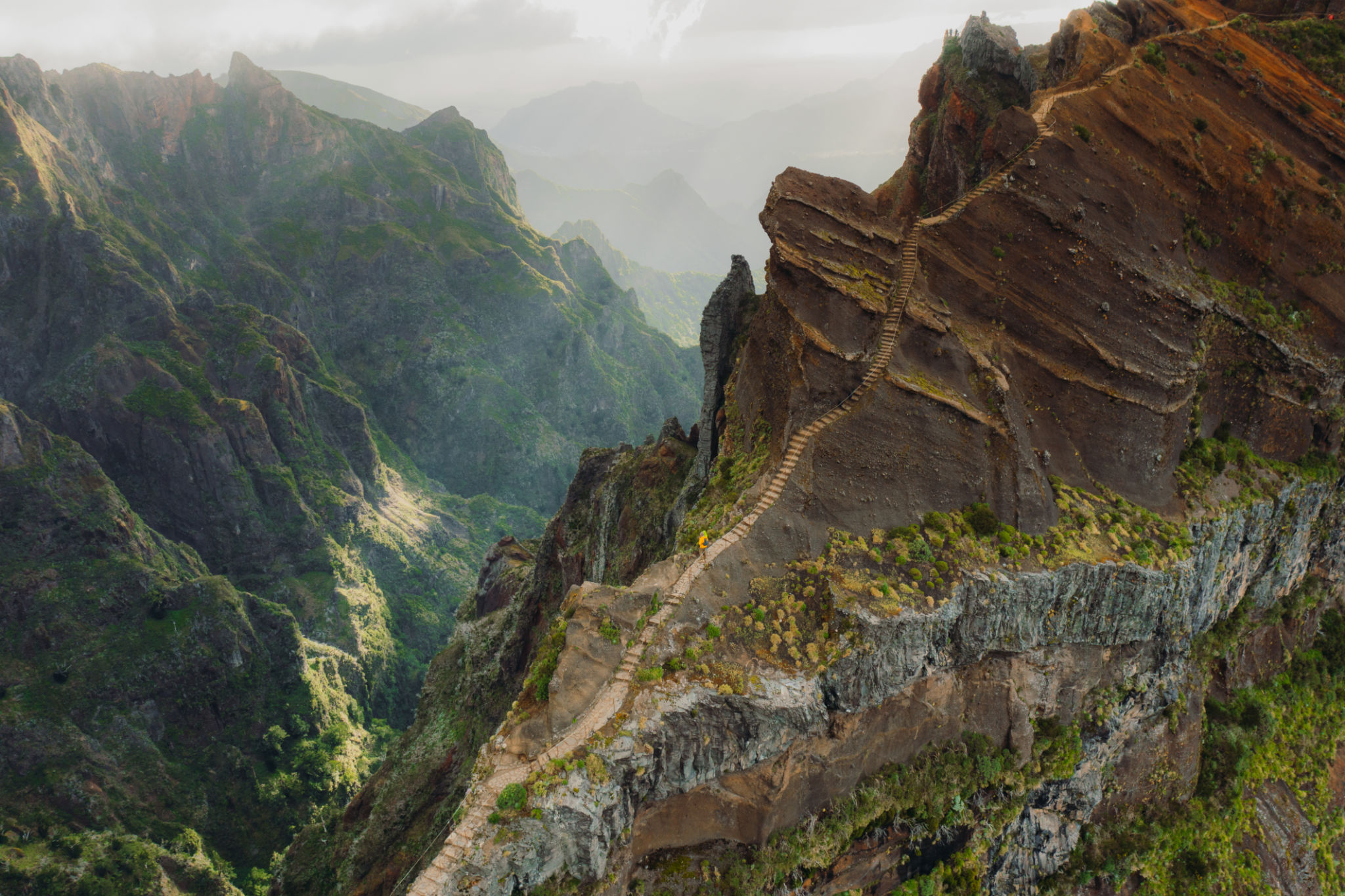 Aerial View of Woman and Man Hiking on Staircase at Dramatic Extreme Mountain Terrain of Madeira Island Aerial View of Woman and Man Hiking on Staircase at Dramatic Extreme Mountain Terrain of Madeira Island