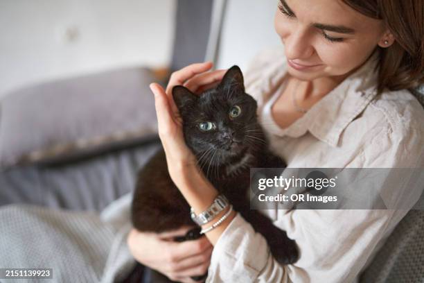 woman holding cute black cat at home - una mujer de mediana edad solamente fotografías e imágenes de stock