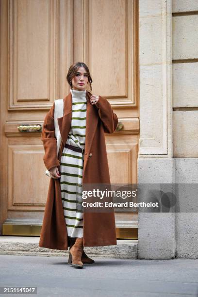 Heart Evangelista wears earrings, a brown long oversize trench coat, a black and white turtleneck striped long dress, a leather belt, a white leather...