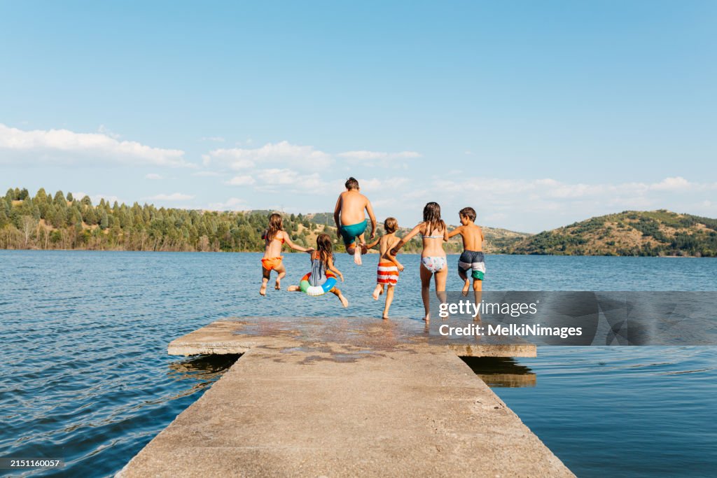 Children having fun jumping from a pier in to the lake on a hot summer day