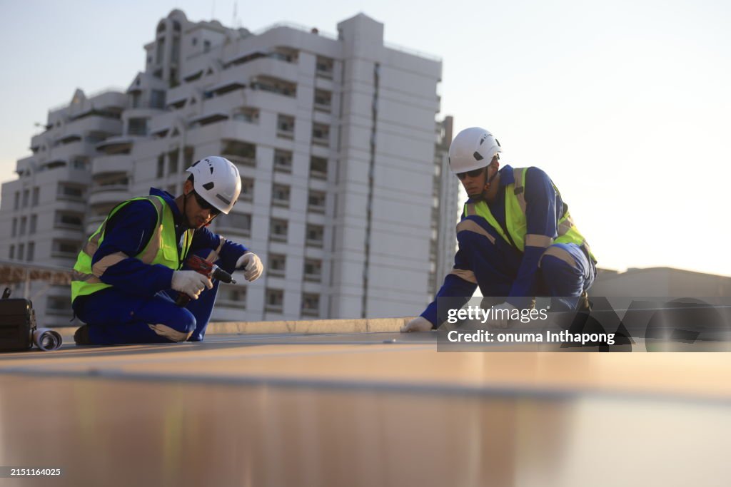 Aerial view of two solar engineers working on the roof of a building in a large city