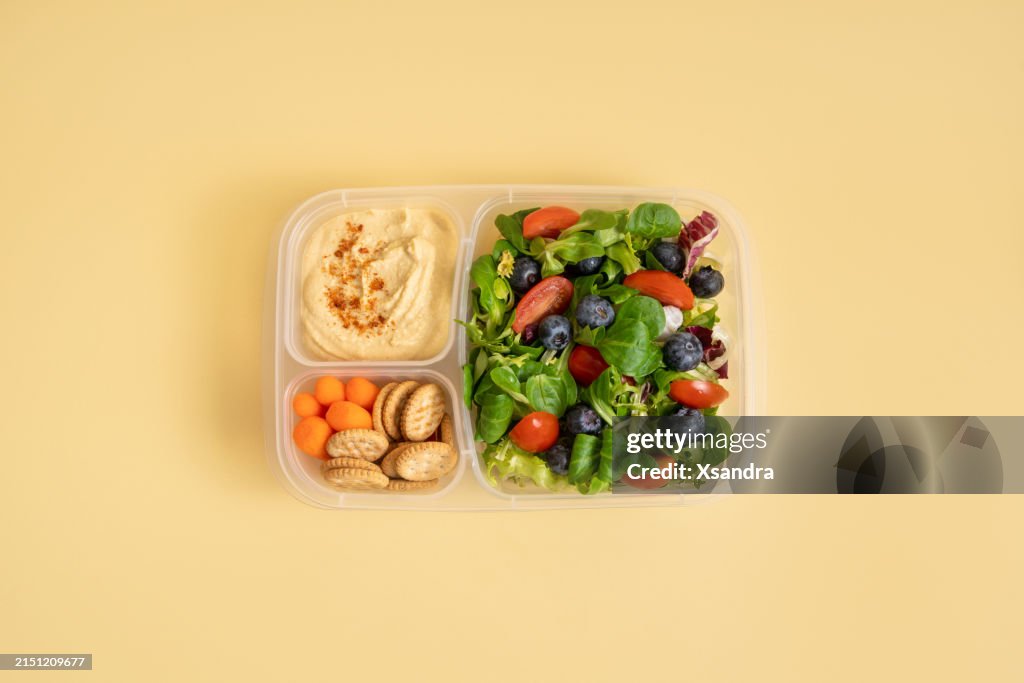 Lunch box with salad and hummus on yellow background