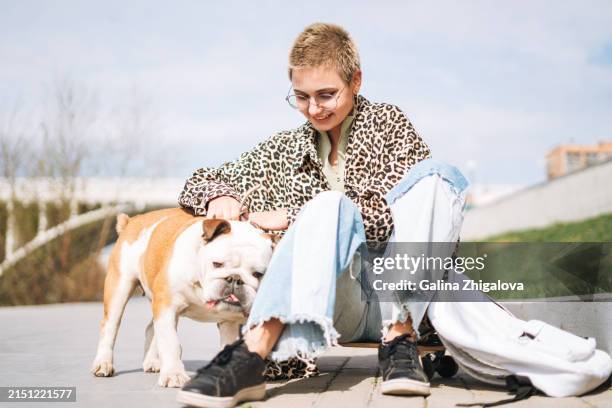 Smiling Teenage Girl In Glasses With Short Hair In Leopard Jacket With Her Dog Against City Street High-Res Stock Photo