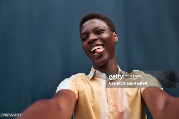 cheerful young man sticking tongue out taking selfie - een gek gezicht trekken stockfoto's en -beelden