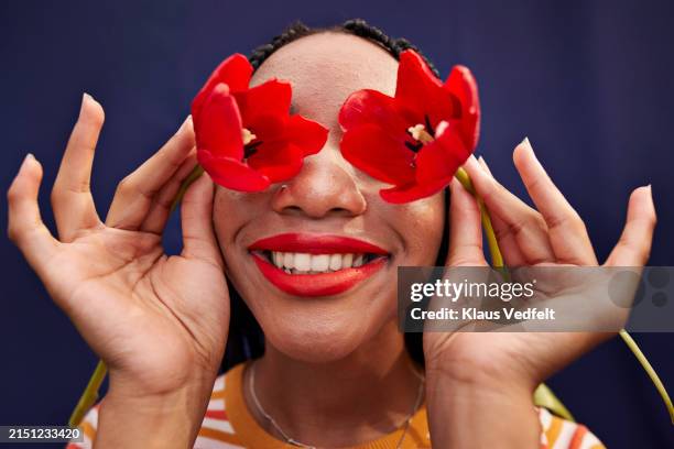 smiling girl covering eyes with fresh red tulip flowers - obscured face stock pictures, royalty-free photos & images
