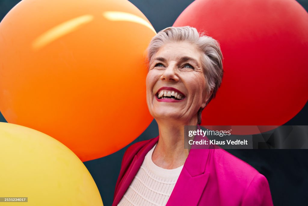 Happy senior woman with balloons looking up