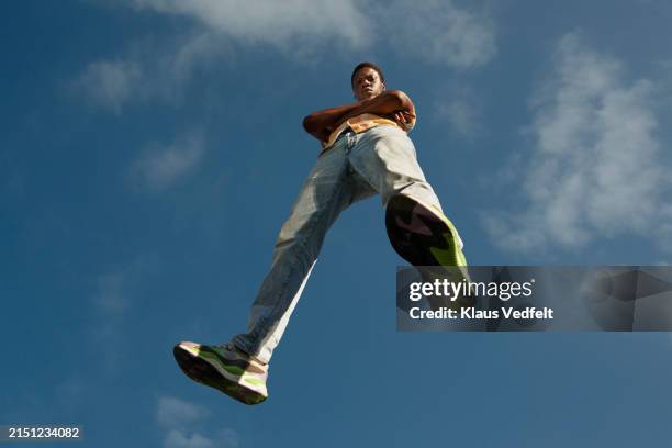 confident young man with arms crossed flying mid-air - blue shoe stock pictures, royalty-free photos & images