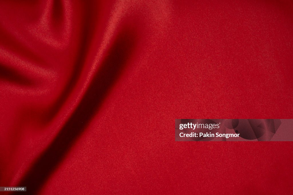 Red silk silky satin fabric. Wavy shiny luxurious shine drapery background, material texture. Full frame.