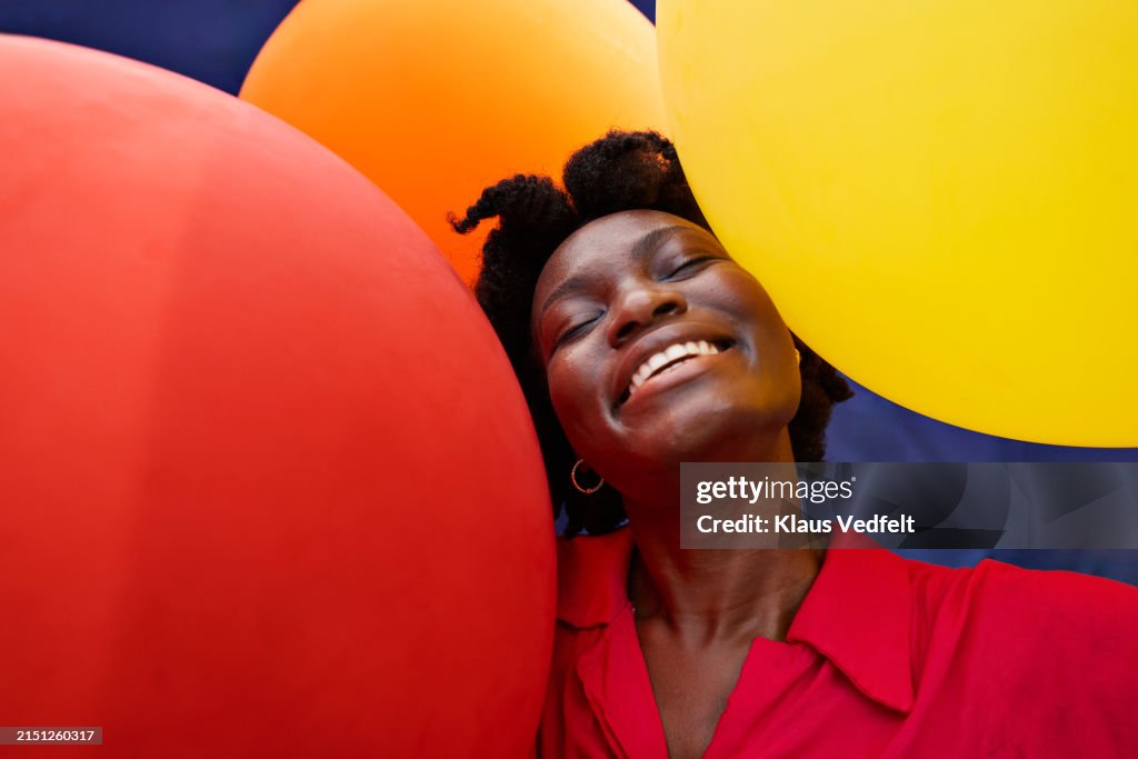 Happy young woman with eyes closed amidst balloons