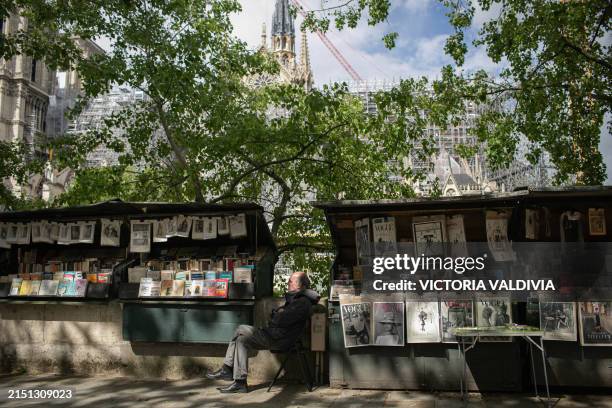 Bouquiniste sitting at his stall with the view of the Notre Dame Cathedral in Paris, France on May 3, 2024. The reconstruction, which aims to be...