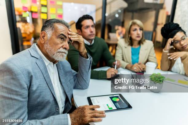 worried senior businessman listening presentation with coworkers during business meeting at office - pressão física imagens e fotografias de stock