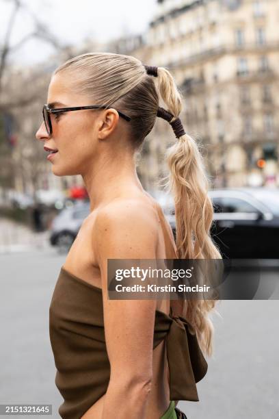 Caroline Daur wears a Miu Miu scarf top, oversized sunglasses with orange lenses and a double pony tail in her hair outside the Miu Miu show during...
