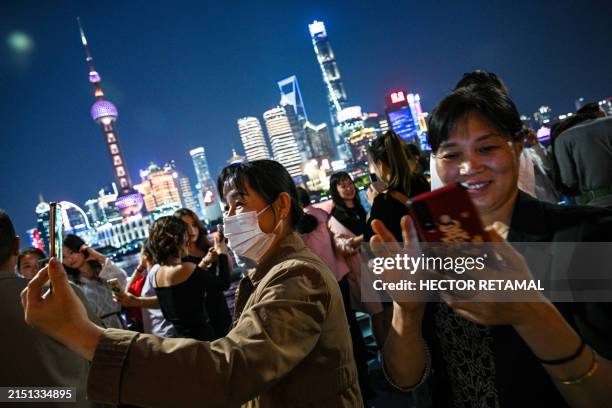 People visiting the Bund promenade take pictures along the Huangpu river in Shanghai on May 7, 2024.