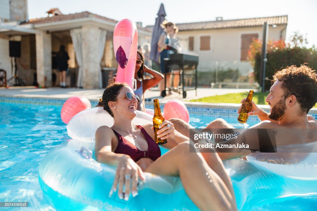 Carefree Young Couple Spending A Hot Summer Day In The Pool Drinking Beer