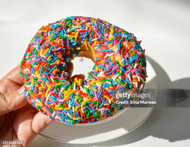 hand holding rainbow sprinkle donut - hundreds and thousands stock pictures, royalty-free photos & images