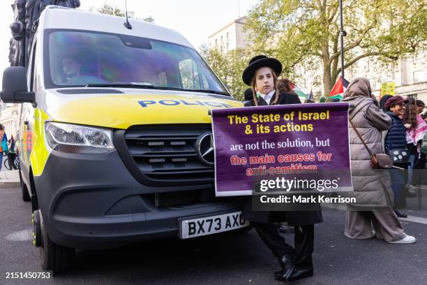 Young ultra-Orthodox Jew from Neturei Karta holds a sign in front of a stationary Metropolitan Police vehicle during a Hands Off Rafah demonstration...