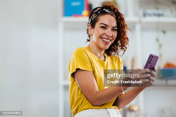 smiling woman in yellow top using smartphone indoors - camisa amarela imagens e fotografias de stock
