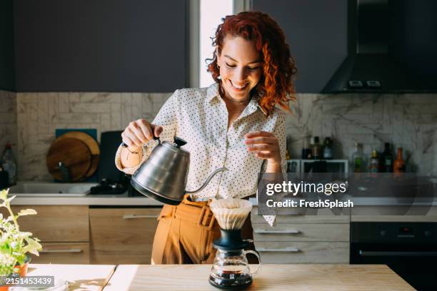 happy woman brewing coffee in a sunlit modern kitchen - steep stock pictures, royalty-free photos & images