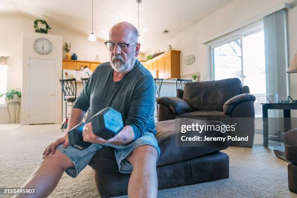 focused mature man curling a 20-pound hand weight for a home fitness workout - hand weight stock pictures, royalty-free photos & images