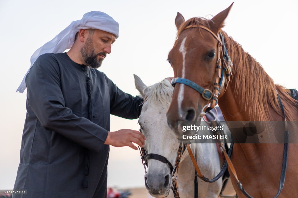 Arab Man in Traditional Clothing Petting his Horses in the Dubai Desert