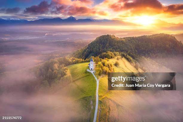 view from above of the serene beauty of the small church of st. primoz in jamnik caressed by the fog at sunrise on green hill in slovenia, kranj, gorenjska - eslovenia fotografías e imágenes de stock