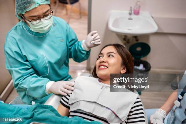 giovane donna sorridente alla clinica dentista con l'assistente in clinica - otturazione dentale foto e immagini stock