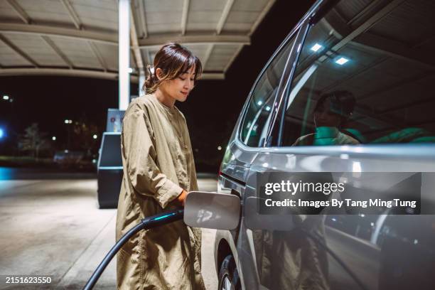 eco-friendly charge: young asian woman holding electric charger plug by car at charging station - sustainable energy stock pictures, royalty-free photos & images