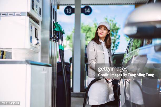 modern mobility: young asian woman fuelling up her car at gas station - petrol station stock pictures, royalty-free photos & images